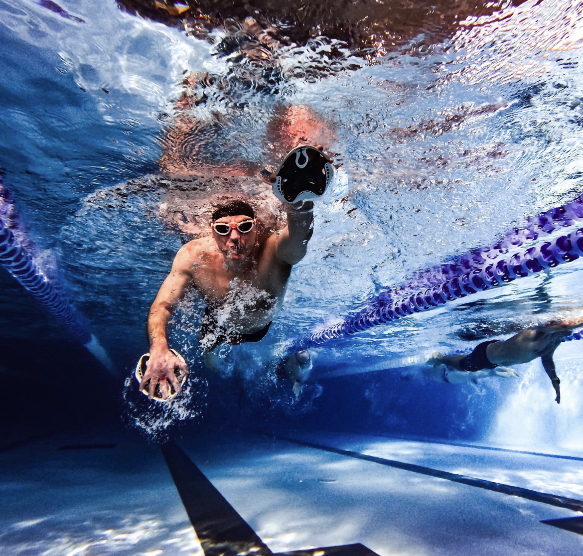 male swimmer pictured from under the water using hand paddles