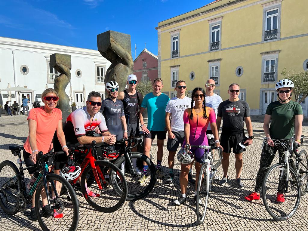Swim 1st Triathlon Club members in a group photo with their bikes in a square in Portugal
